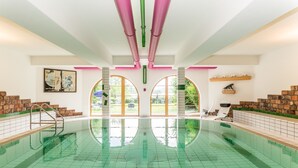 A swimming pool with a tiled floor, a ladder, and a view of the outdoors through arched windows. - Appartementhotel Seespitz (Fuessen)