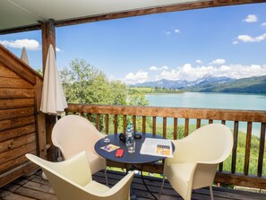 A wooden deck with two chairs and a table, overlooking a lake with mountains in the background. - Appartementhotel Seespitz (Fuessen)