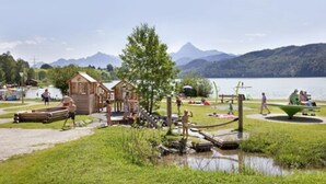 A lakeside park with wooden cabins, a playground, and a picnic area. - Appartementhotel Seespitz (Fuessen)