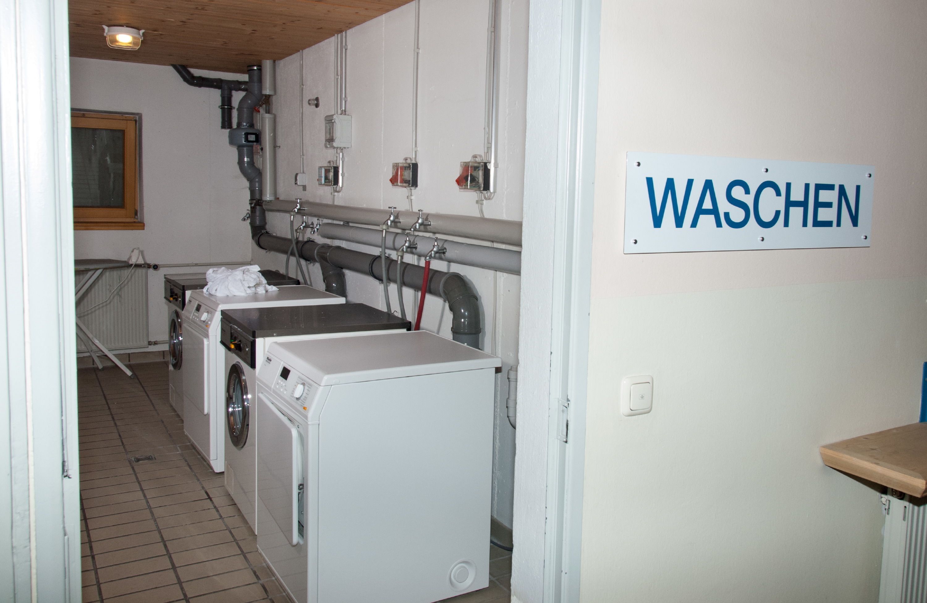 Ein Waschraum mit zwei Waschmaschinen, einem Schild mit der Aufschrift 'WASCHEN' und einer Heizung an der Wand.
