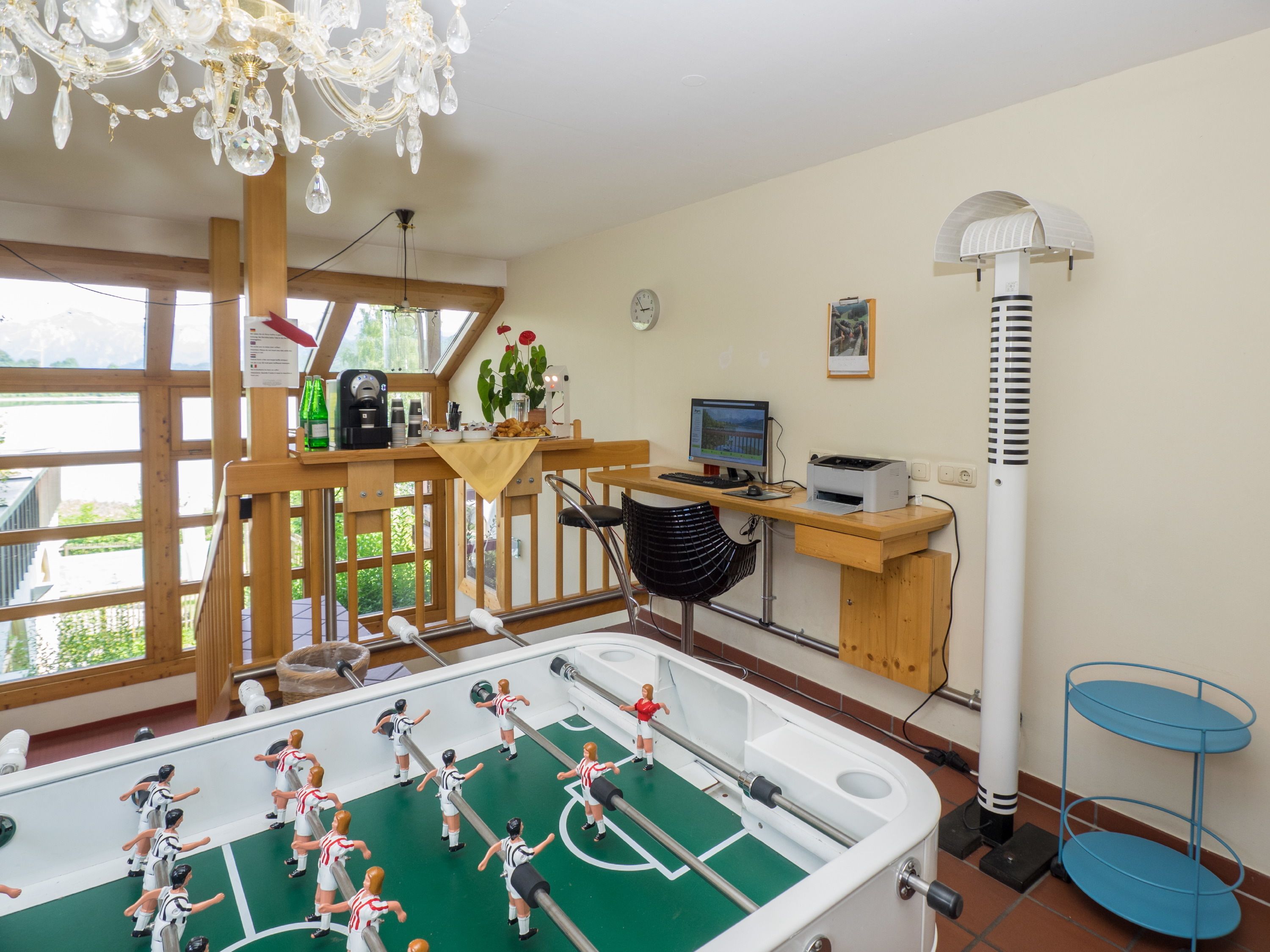 Ein Zimmer mit einer Fußballstoßmaschine, einem Schreibtisch mit Computer, einem Stuhl und einem Standventilator.