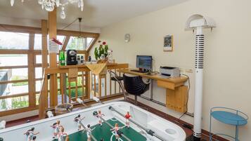 Ein Zimmer mit einer Fußballstoßmaschine, einem Schreibtisch mit Computer, einem Stuhl und einem Standventilator.