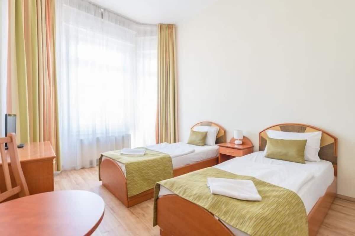 A hotel room with two single beds, a wooden desk, a chair, and a round table.