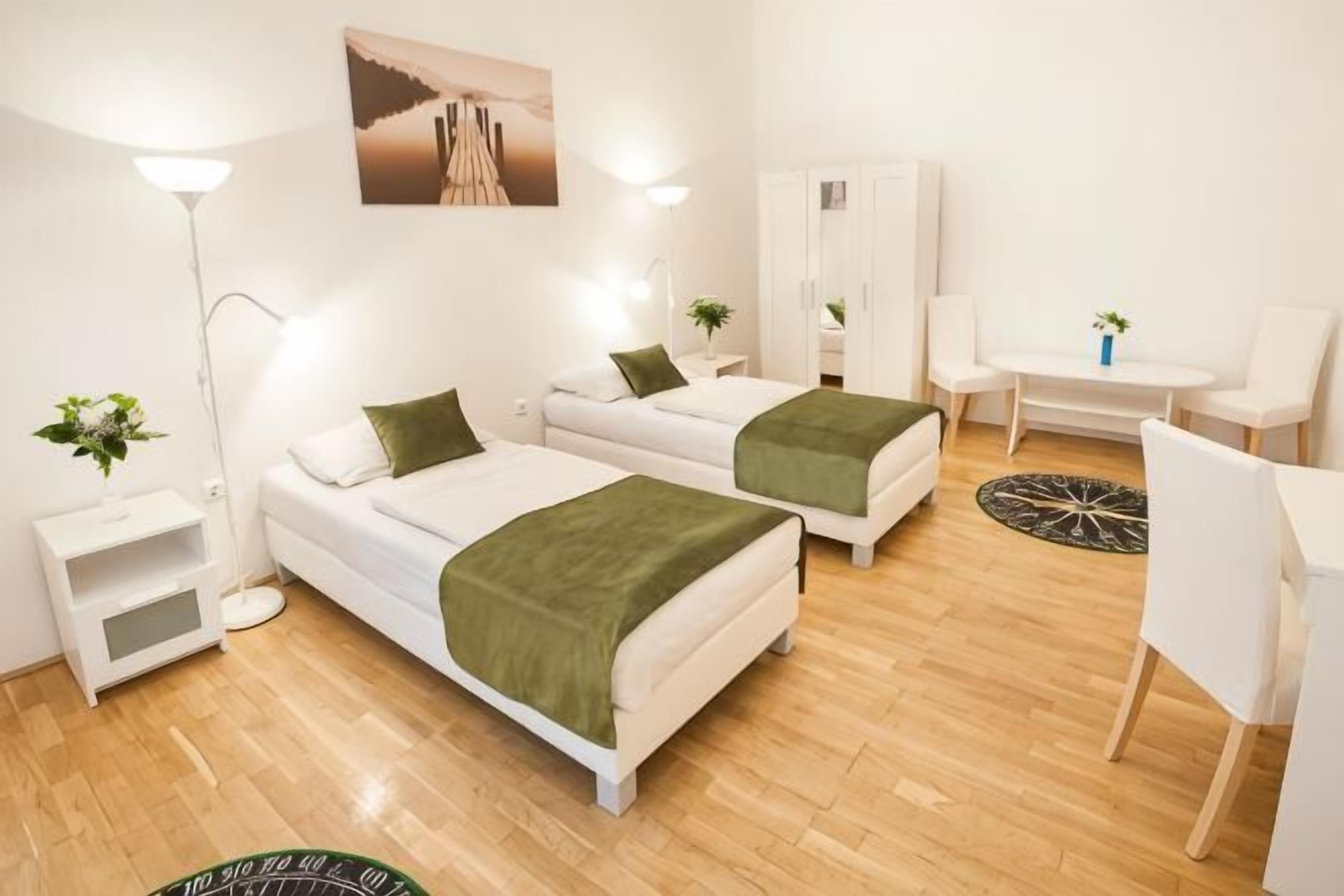A hotel room with two beds, a desk, a chair, a wardrobe, and a lamp.