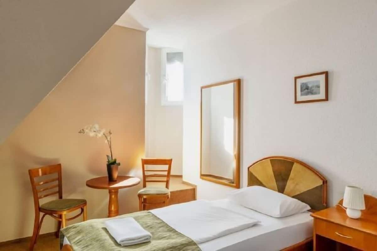 A hotel room with a bed, a chair, a small table, a lamp, a mirror, and a framed picture on the wall.