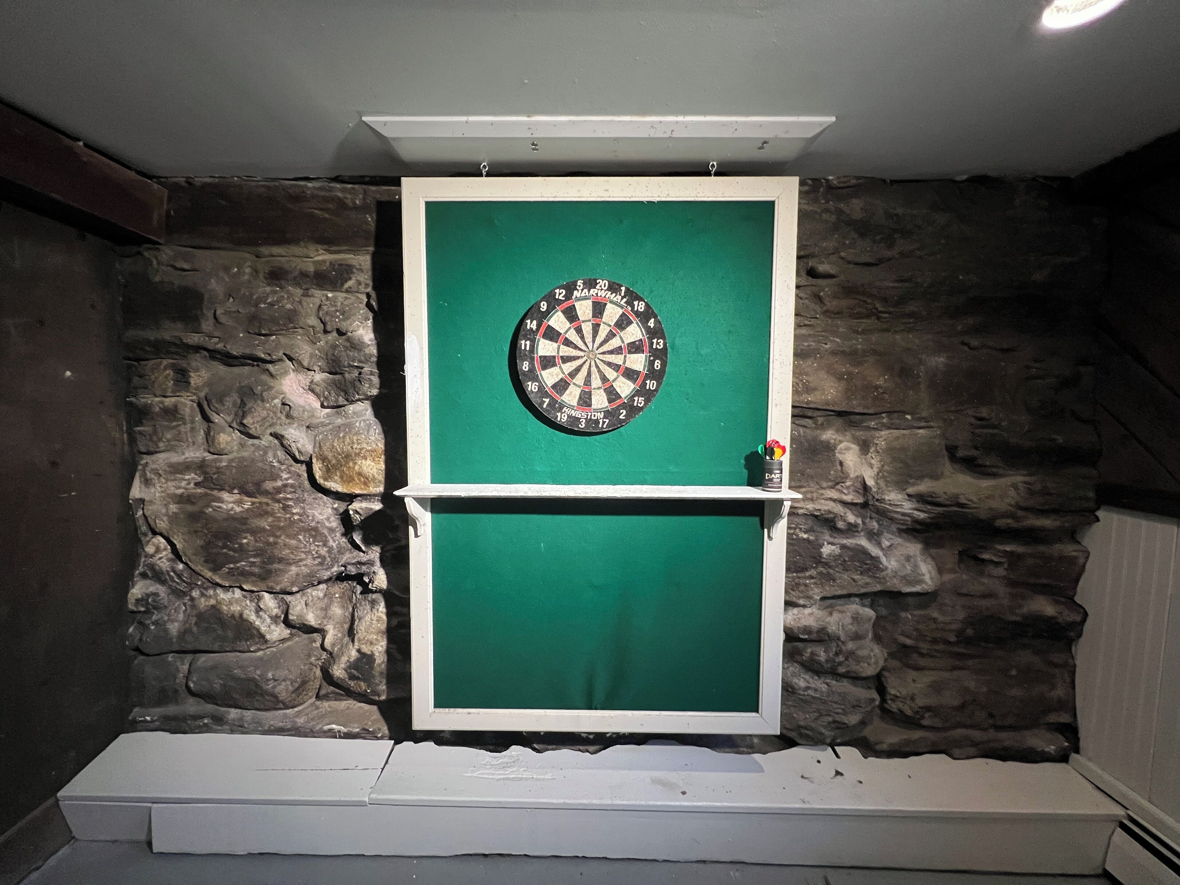 Dartbord bevestigd aan een groene deur, met een stenen muur op de achtergrond.