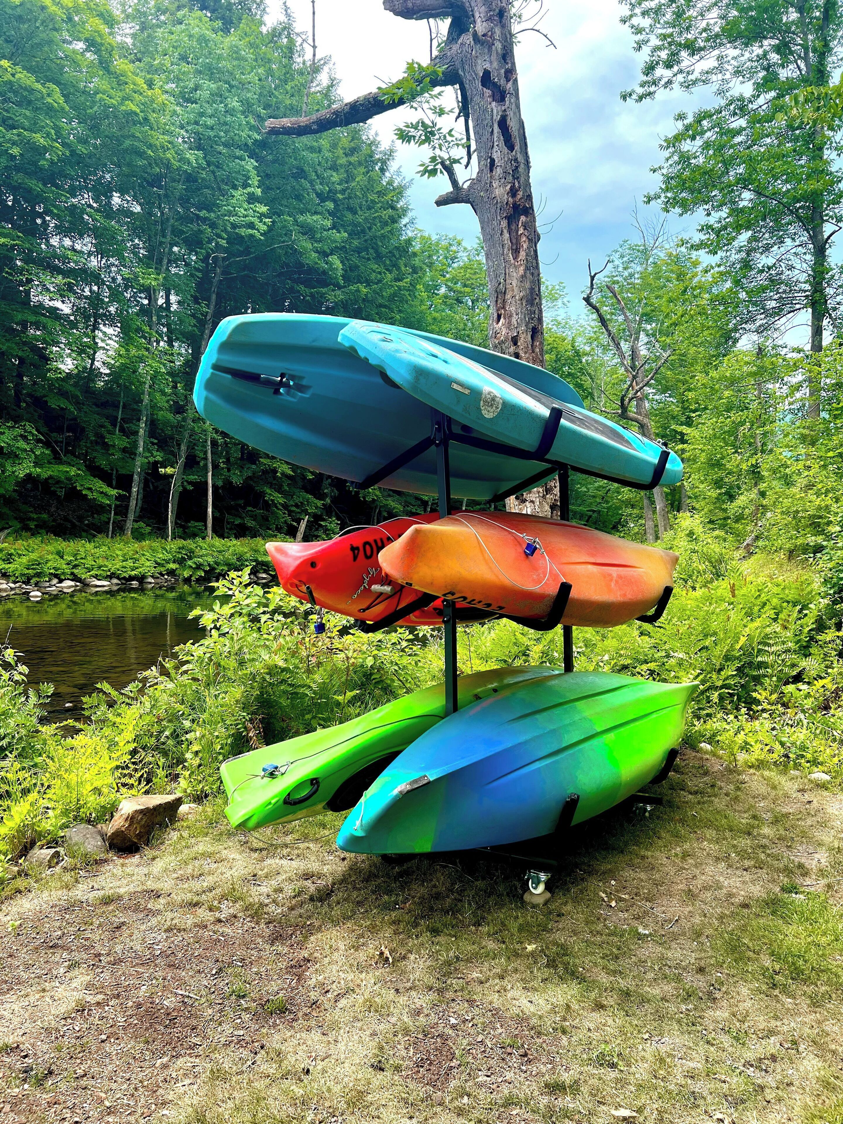A stack of kayaks on a stand near a pond surrounded by trees.