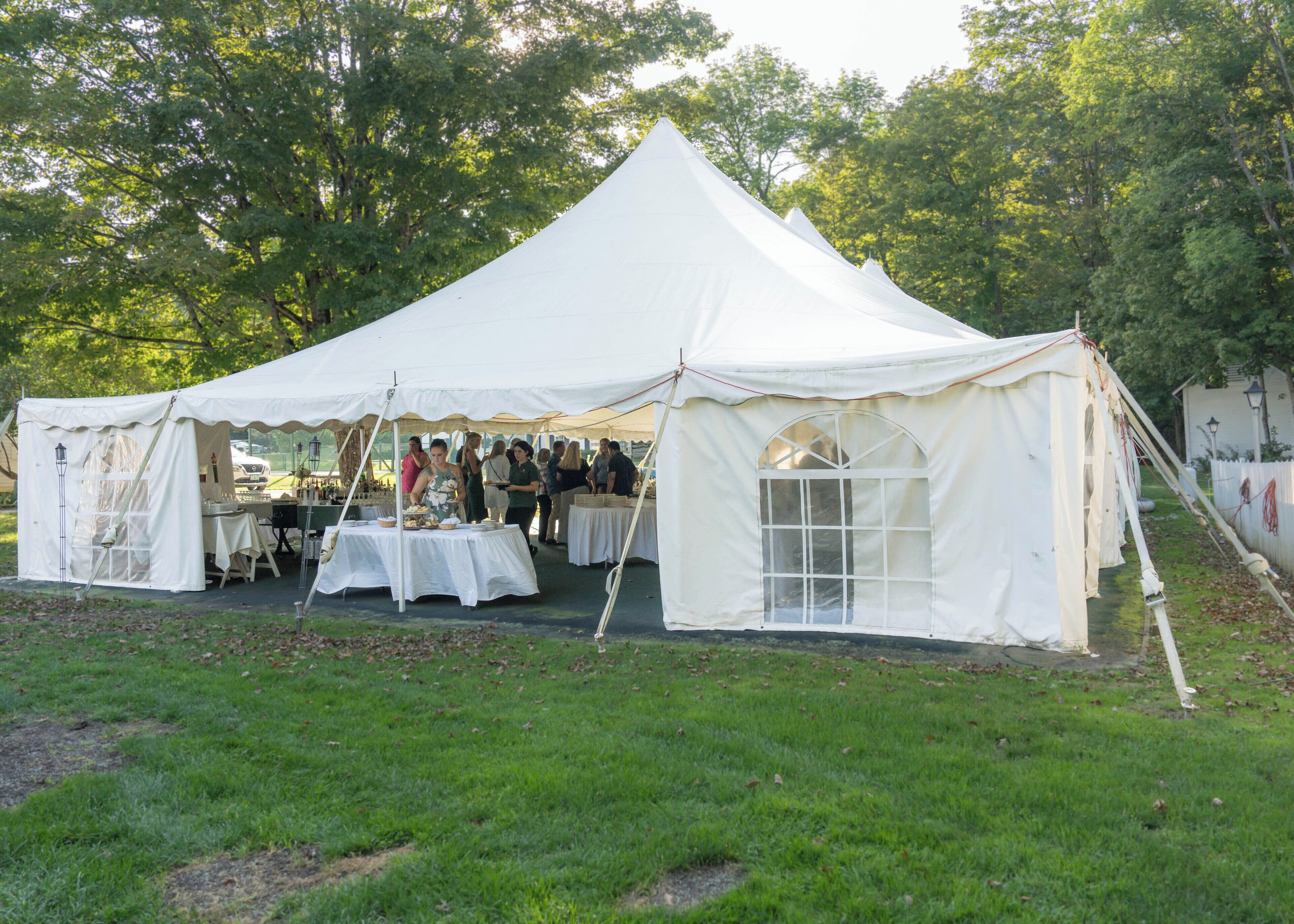 A white tent with tables set up inside, surrounded by a grassy area and trees.