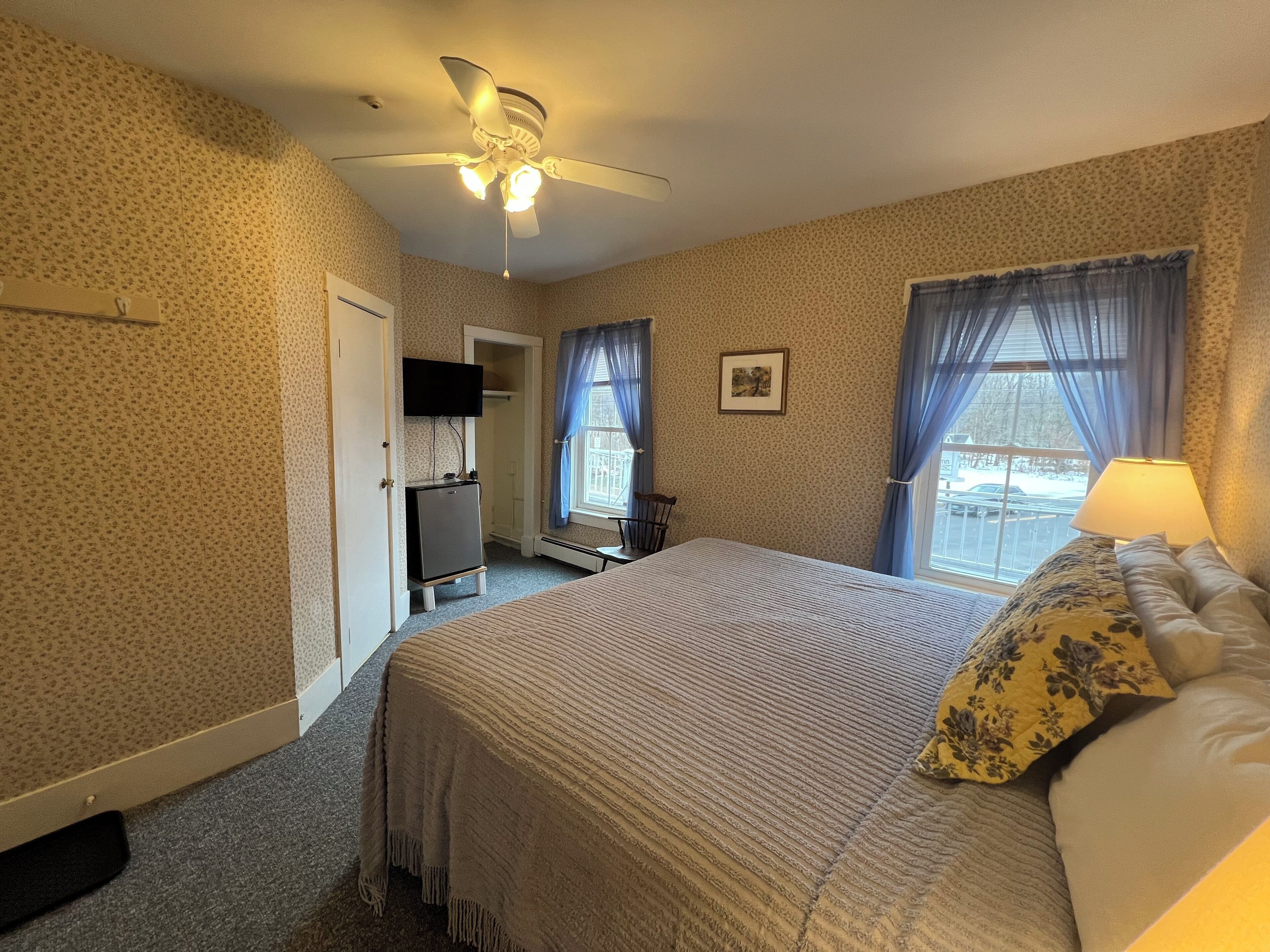 A bedroom with a bed, a ceiling fan, a desk, a chair, and a window with curtains.