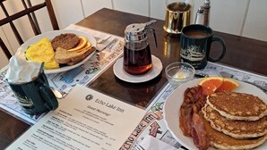 Ein Esstisch mit Speisekarte, Kaffeekanne, Tasse und einem Teller Pfannkuchen und Speck.