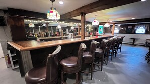 Eine Bar mit Holztresen, Lederbarkreühlen und hängenden Buntglasleuchten.