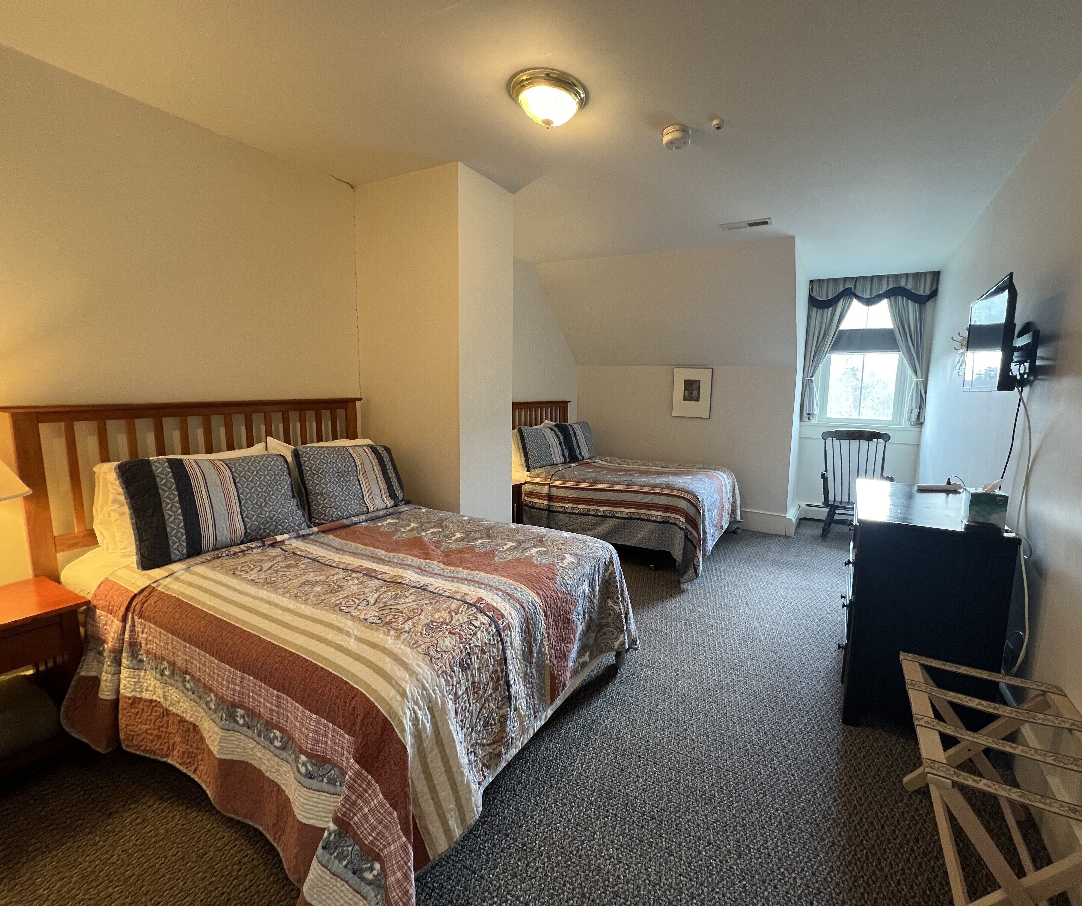A bedroom with two beds, a desk, a chair, and a window with curtains.