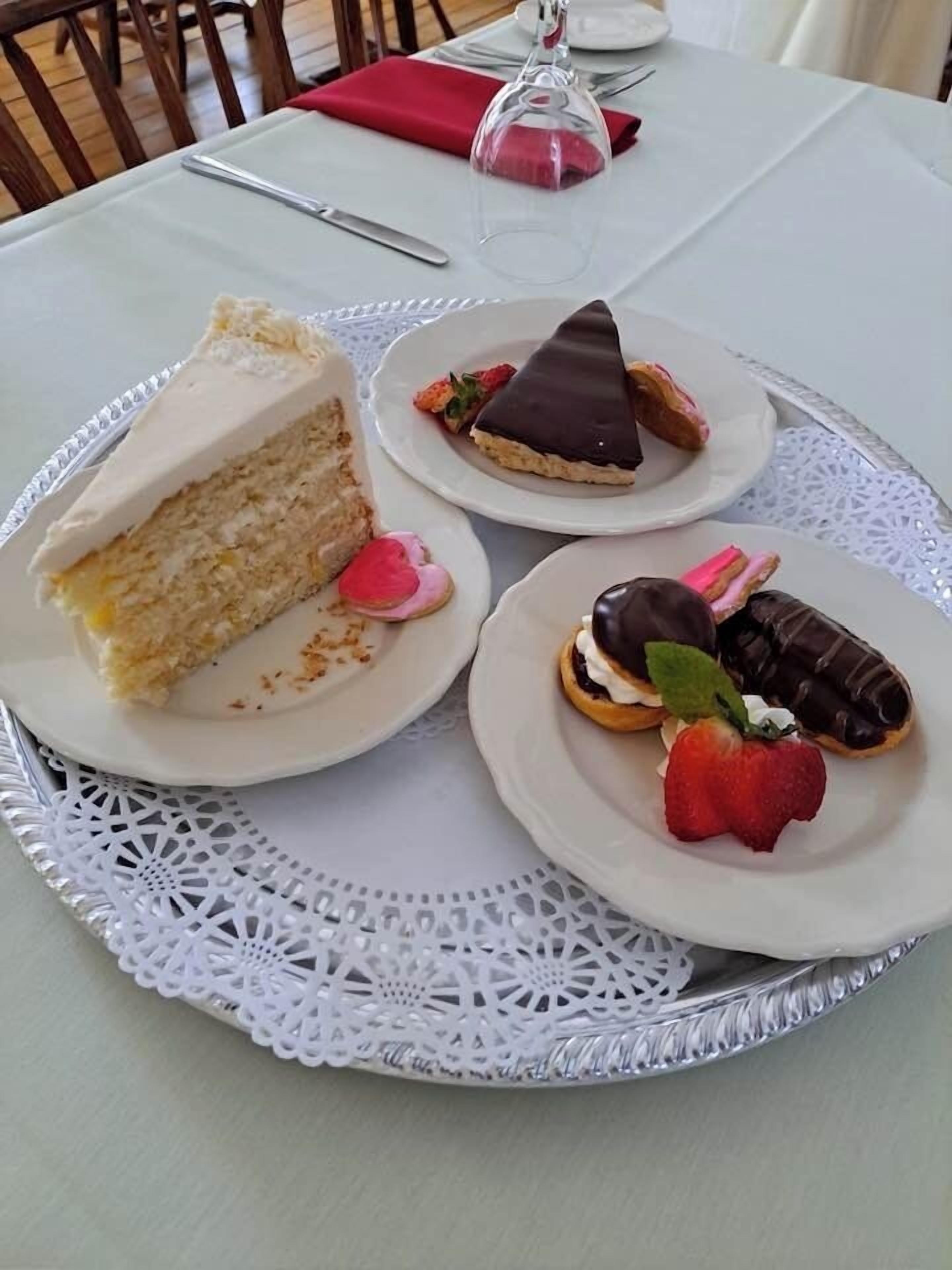 A table with a white tablecloth and a lace doily. There are three plates with desserts, a wine glass, and a red napkin.