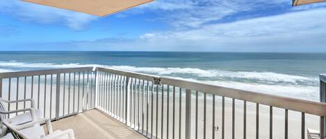 A balcony with a view of the ocean, white railings, and two white chairs.
