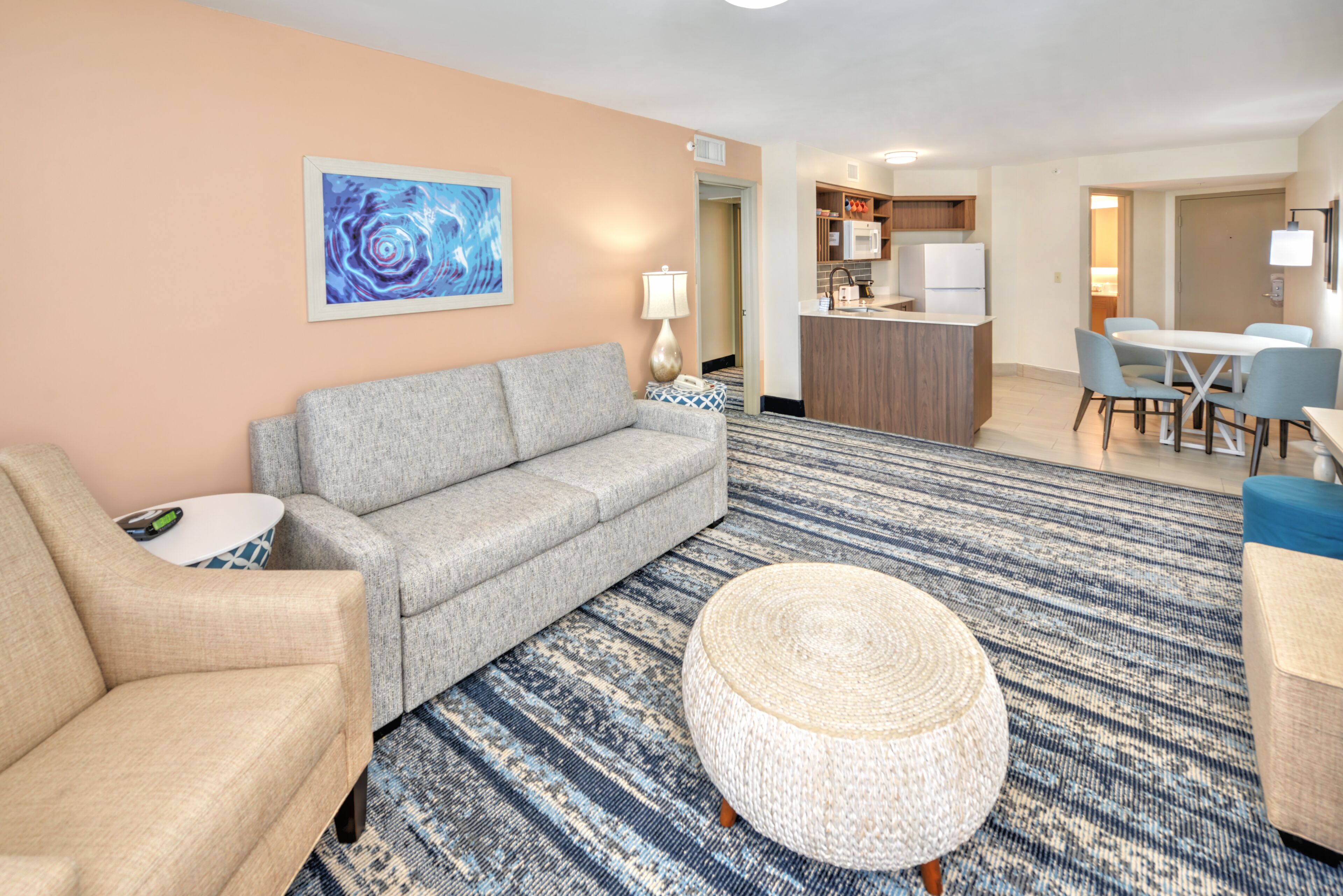 A modern living room with a grey sofa, a round ottoman, and a blue patterned rug.