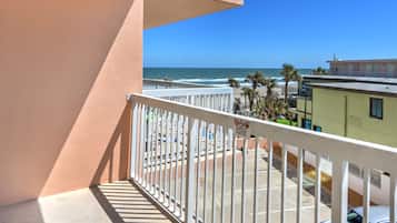 Un balcón con vista a la playa, palmeras y un estacionamiento.