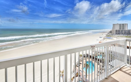 A beach view from a balcony with a pool and lounge chairs.
