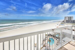 A beach view from a balcony with a pool and lounge chairs.