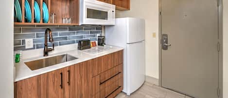 A kitchen with wooden cabinets, a white microwave, a white refrigerator, and a tiled backsplash.