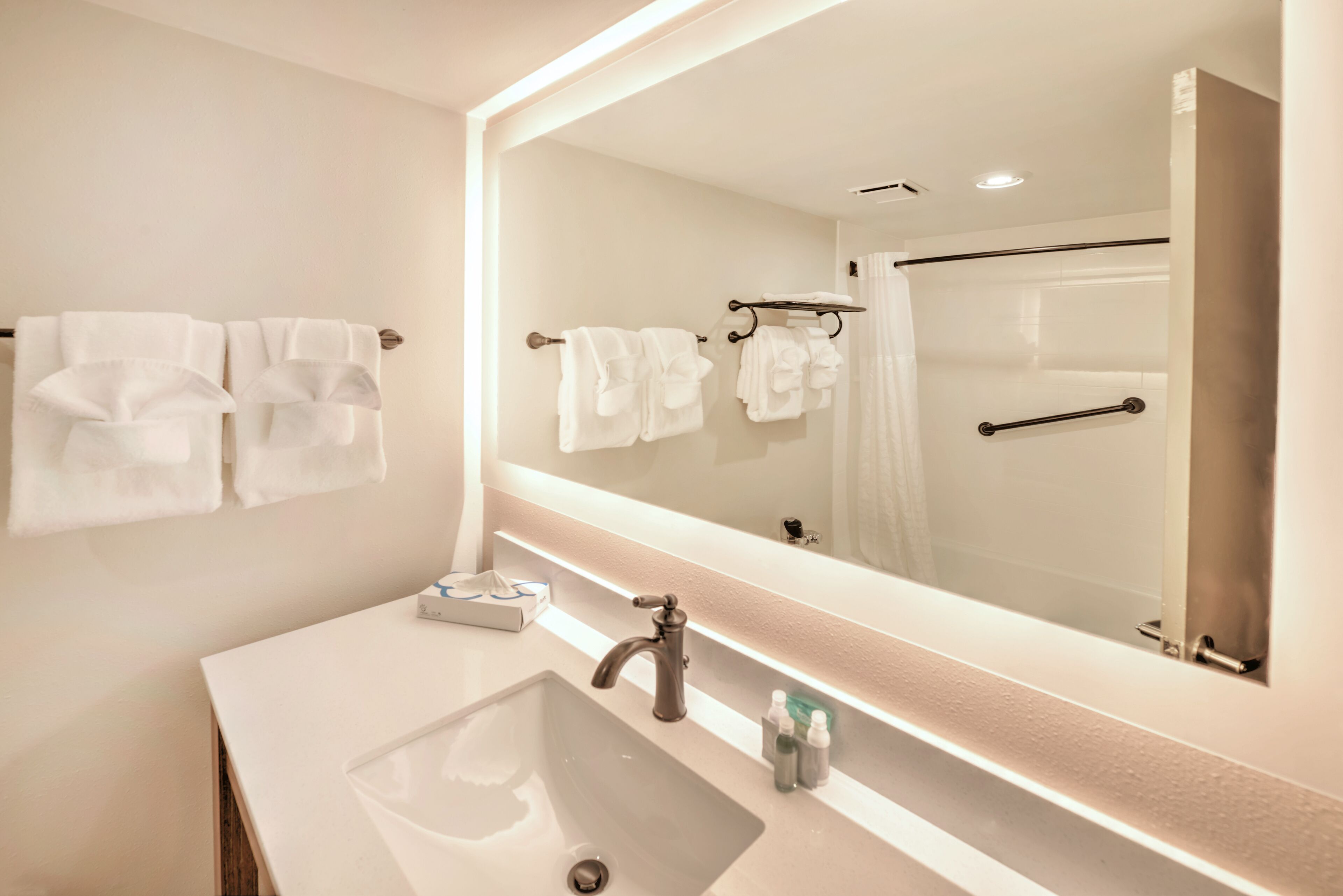A modern bathroom with a large mirror, a sink, and two towel racks.