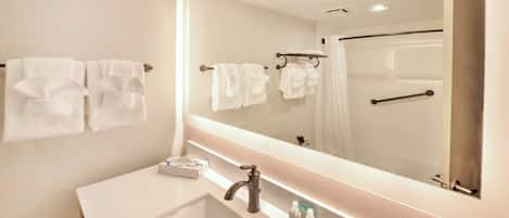 A modern bathroom with a large mirror, a sink, and two towel racks.