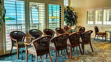 A room with wicker chairs arranged around a table, large windows with blinds, and a patterned carpet.