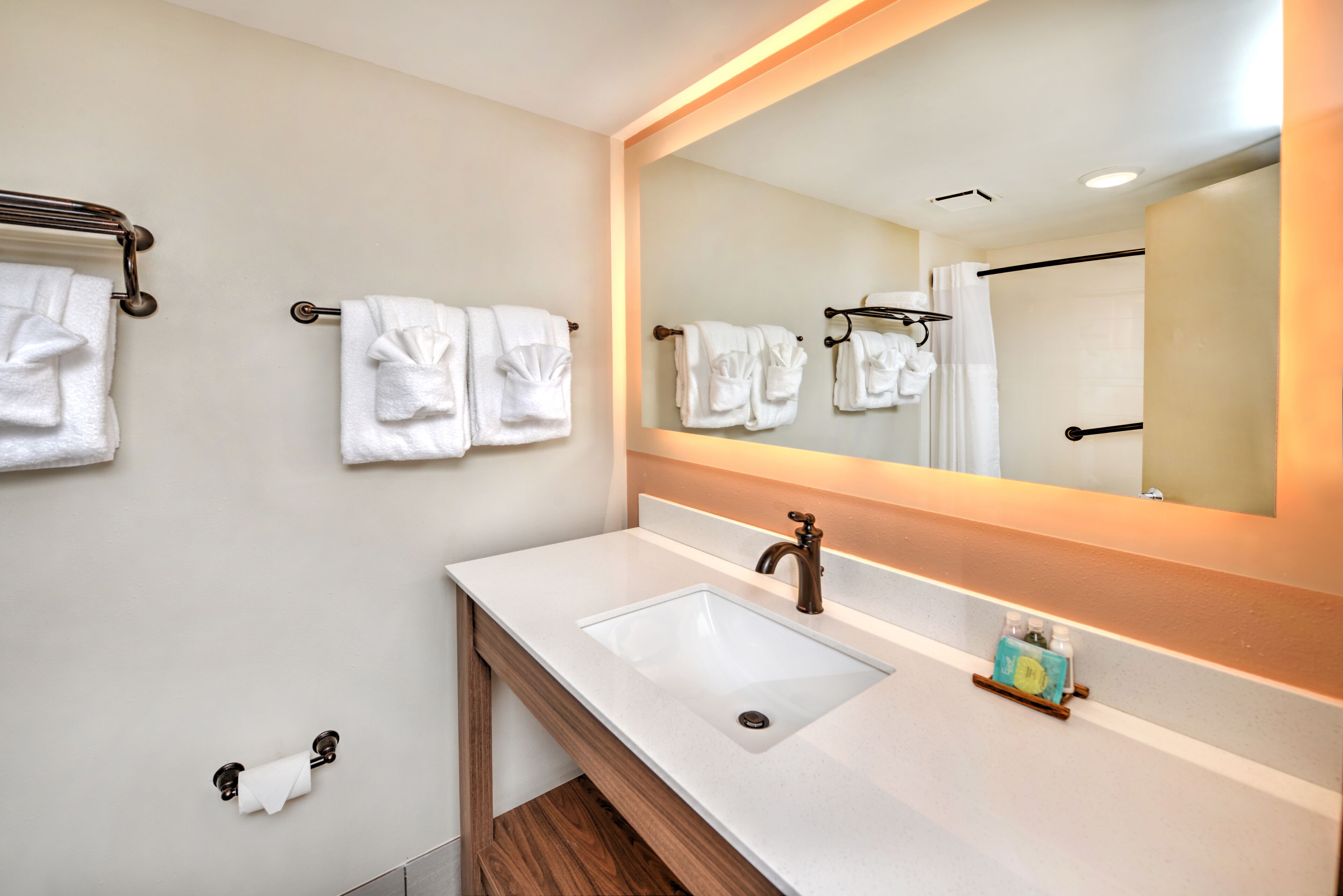 A modern bathroom with a white sink, a large mirror, and multiple towel hooks.