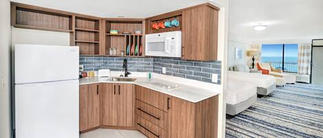 A modern kitchen with wooden cabinets, a white refrigerator, and a microwave. There is a large window with a view of the ocean.