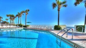 A clear blue pool with a white deck, palm trees, and a view of the ocean. - Bahama House (Daytona Beach Shores)