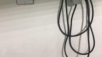 Sinal de estacionamento indicando 'NÃO ESTACIONAR EXCETO DURANTE O CARREGAMENTO' e uma estação de carregamento com cabos.