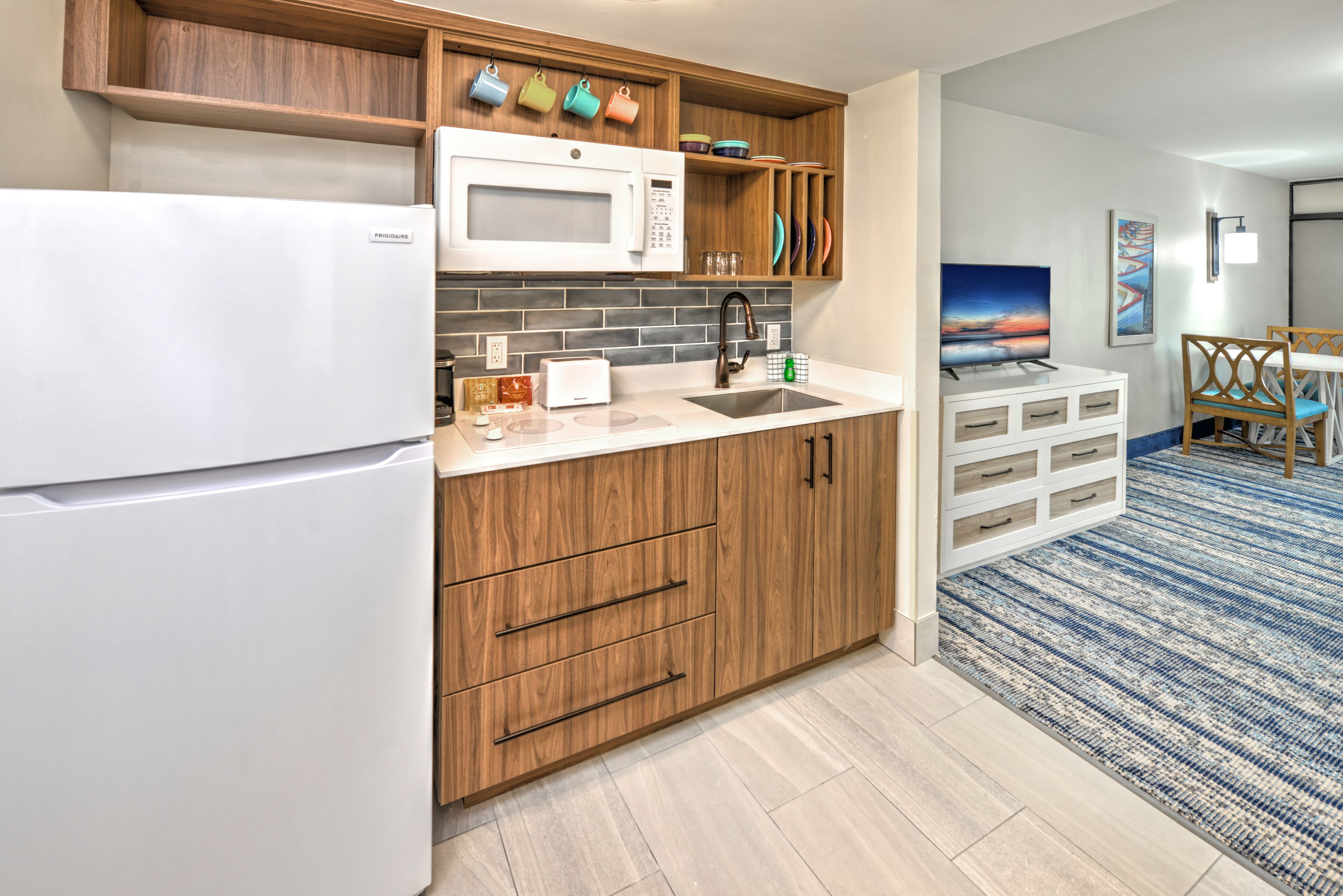 Una cocina moderna con refrigerador, microondas y pileta, armarios de madera y un tapete azul estampado.