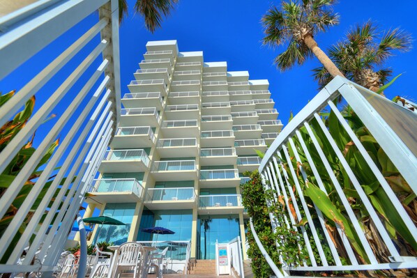 A multi-story hotel with balconies, outdoor seating, and palm trees.