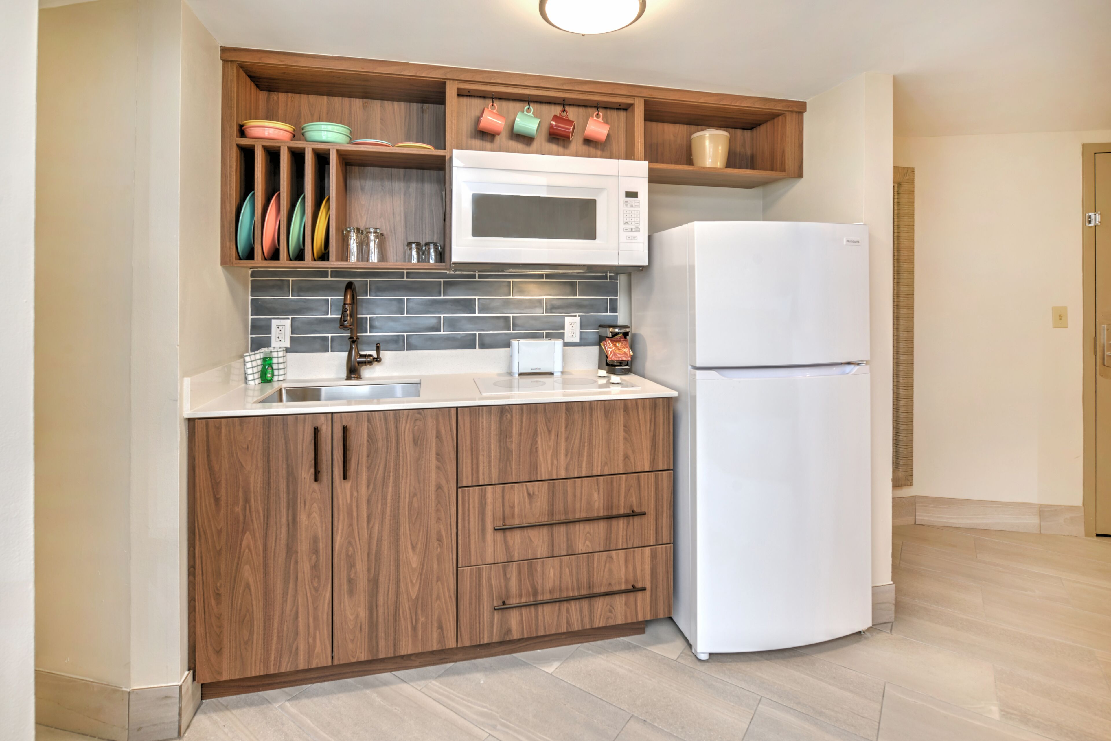 A kitchen with wooden cabinets, a white microwave, a white refrigerator, and a tiled backsplash.