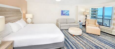 Une chambre d’hôtel avec un grand lit, un canapé, un fauteuil et une vue sur l’océan.