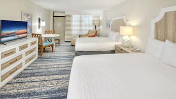 A hotel room with a large bed, a smaller bed, a TV, a desk with a chair, and a window with curtains.