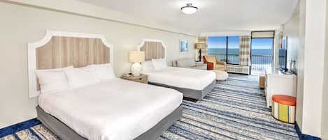 Habitación de hotel con dos camas, un sofá, un televisor y vista al océano.
