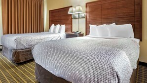 Habitación de hotel con dos camas, cabecera de madera, mesita de noche con lámpara y un ventanal con cortinas.