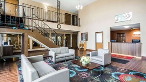 Vestíbulo de hotel con escalera, área de descanso, mostrador de recepción y un reloj.