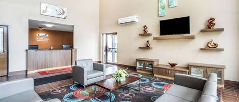 A hotel lobby with a reception desk, seating area, television, decorative wall art, and a patterned carpet.