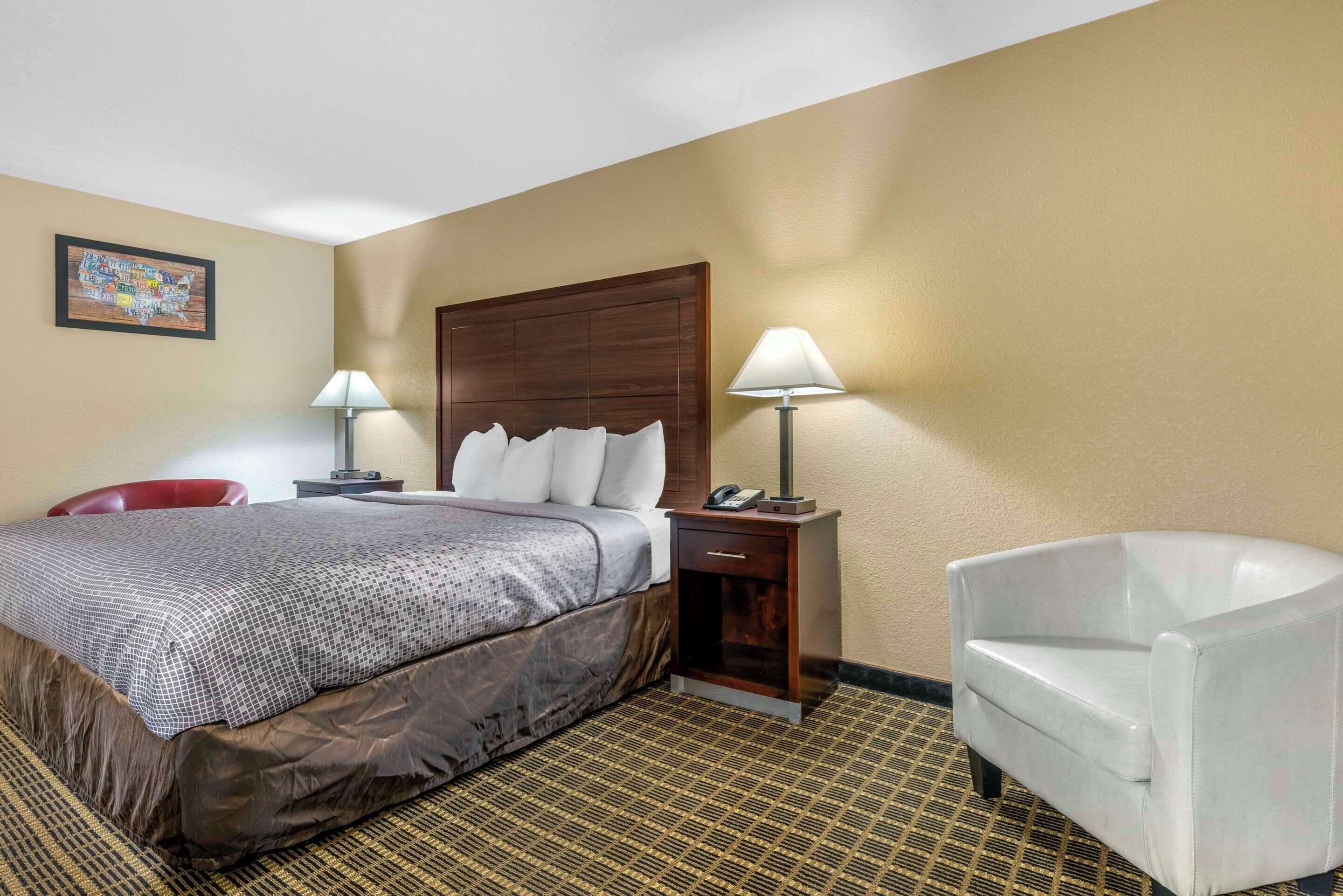 A hotel room with a bed, two bedside tables, a chair, and a wall map.