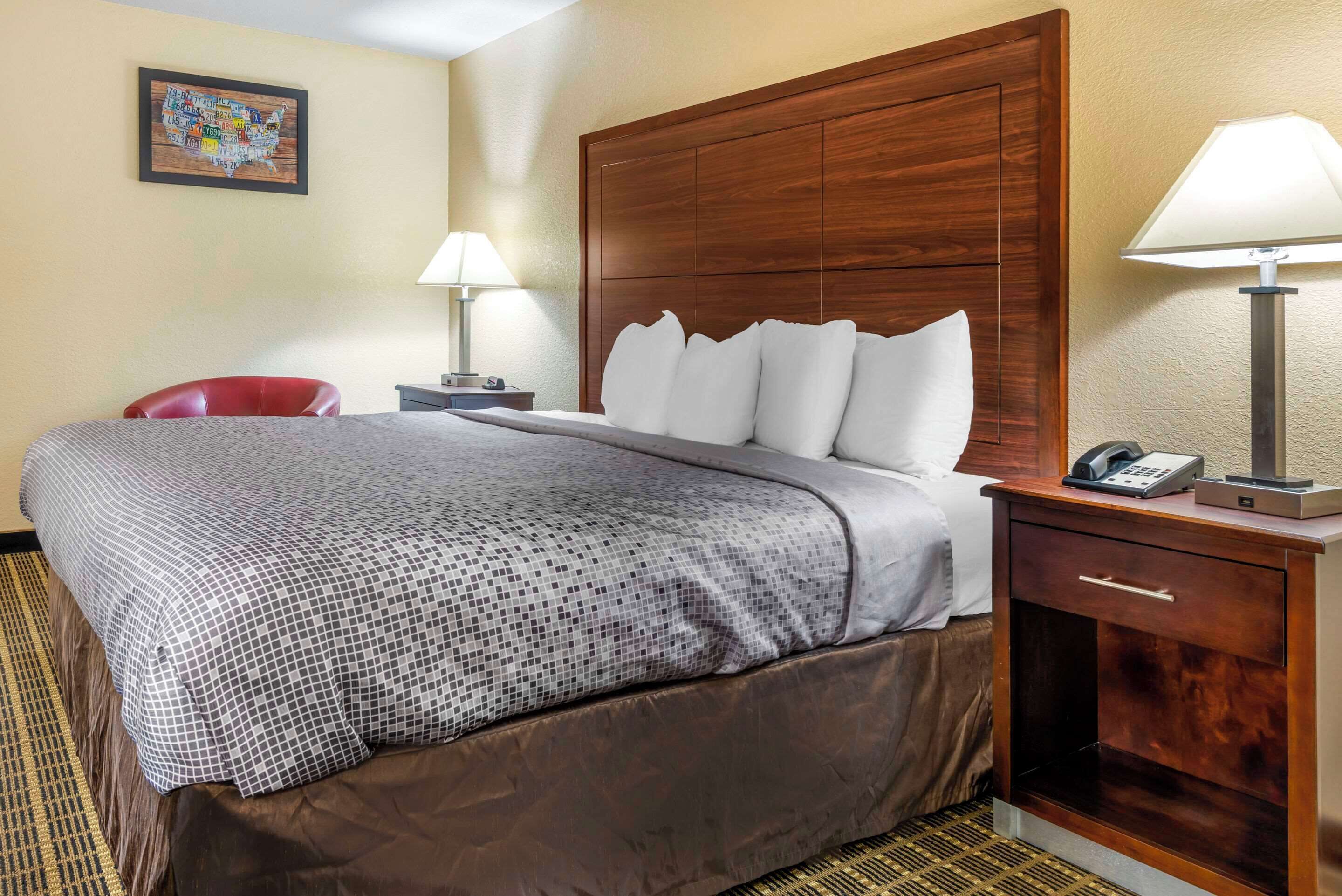A hotel room with a large bed, wooden headboard, two bedside tables with lamps, a red chair, and a wall map.