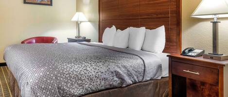 Una habitación de hotel con una cama grande, cabecera de madera, dos mesitas de noche con lámparas, una silla roja y un mapa mural.