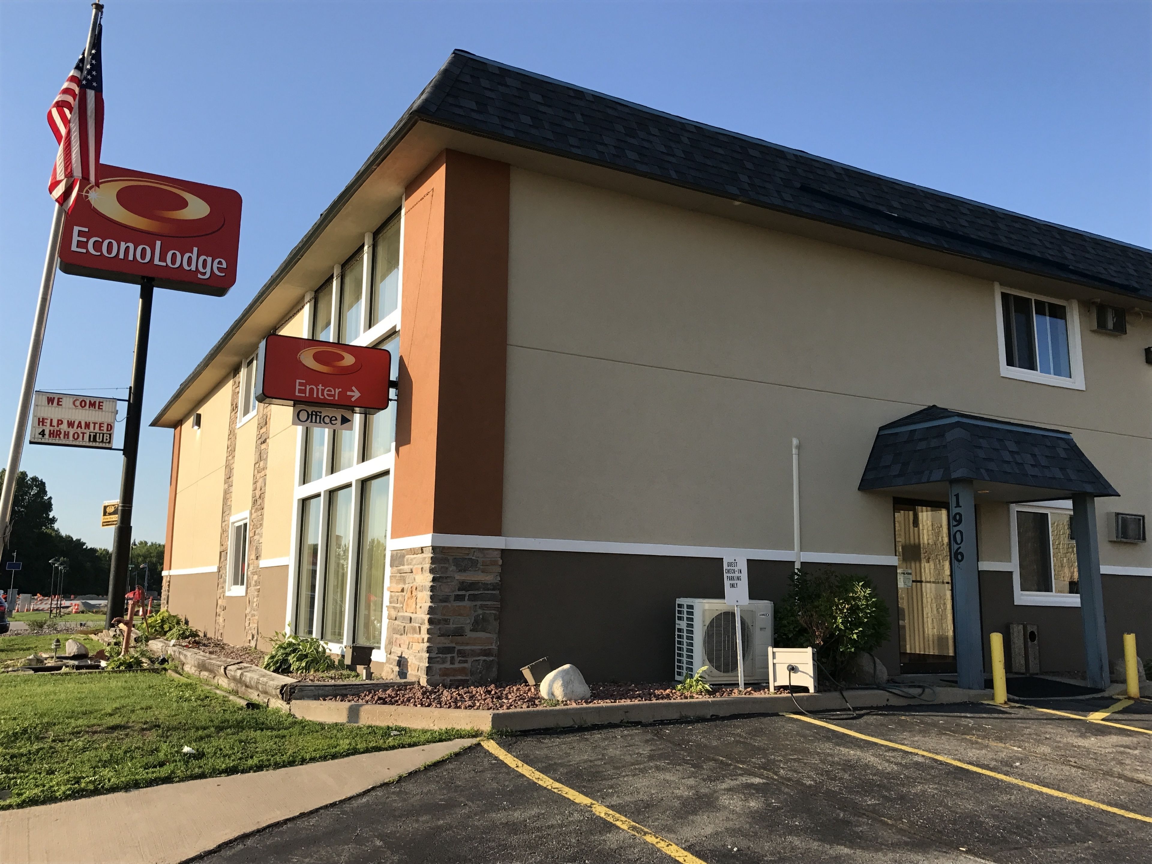 Un edificio su due piani con facciata beige e marrone, un cartello che indica 'EconoLodge' e indicazioni per la reception e l'ingresso.
