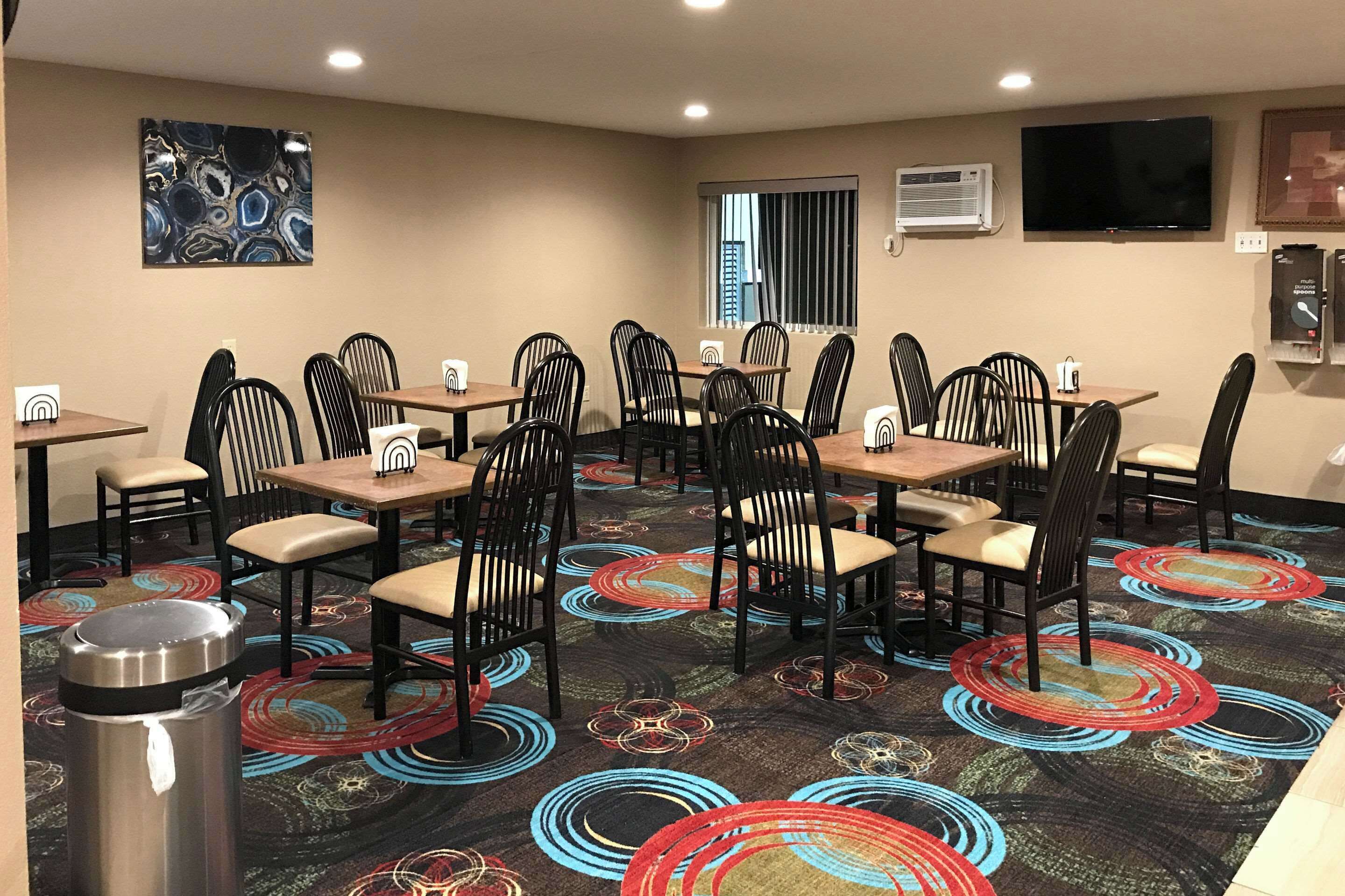 A dining area with tables and chairs, a trash can, and a television on the wall.