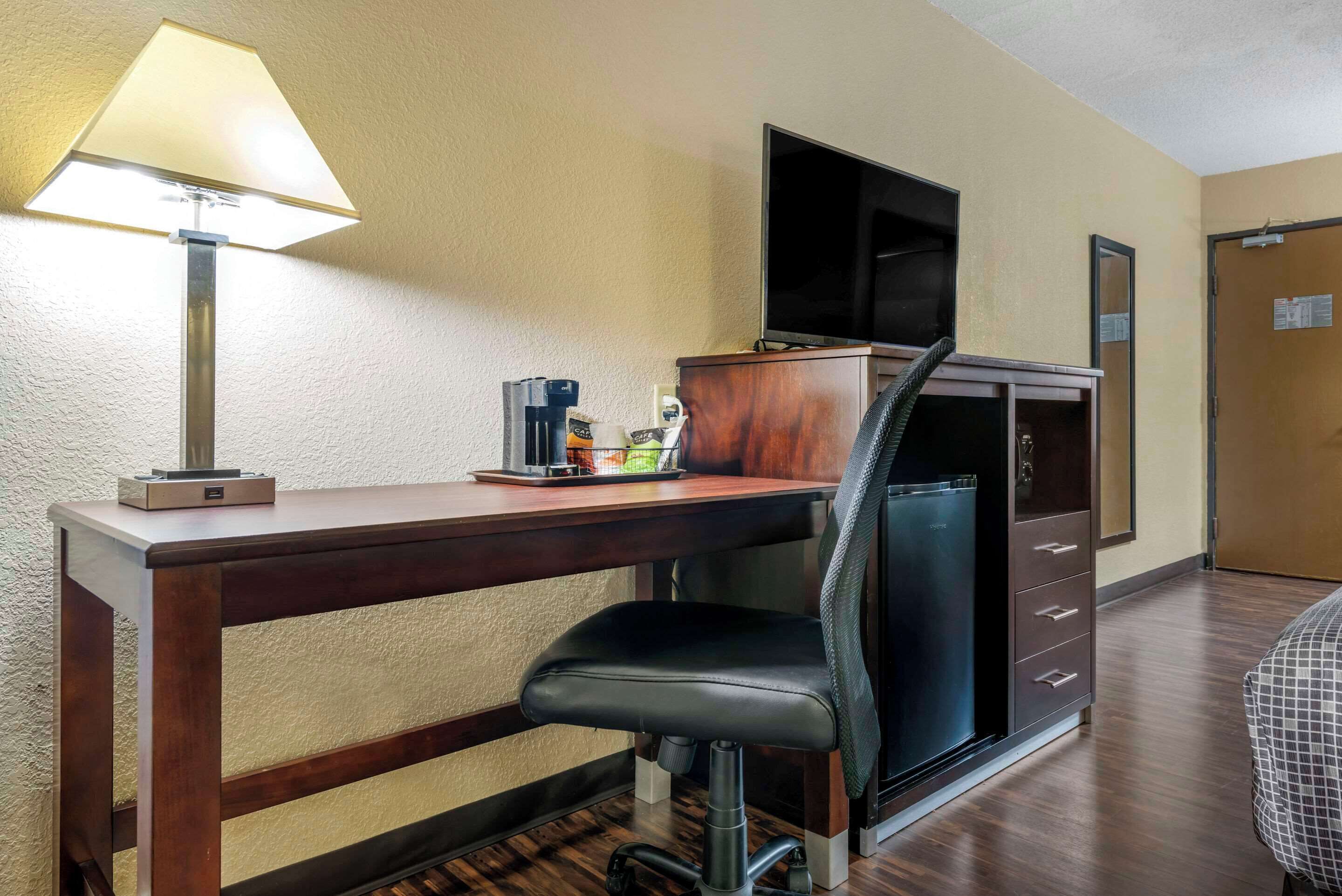 A hotel room with a wooden desk, a black office chair, a television, and a minibar.
