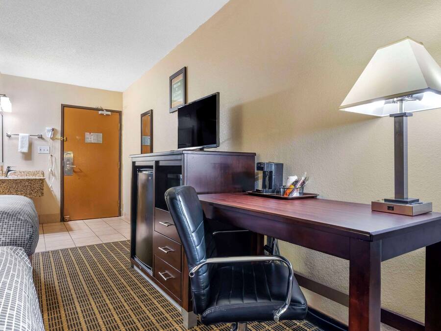 A hotel room with a bed, a desk with a chair, a television, a lamp, and a small table with a tray.