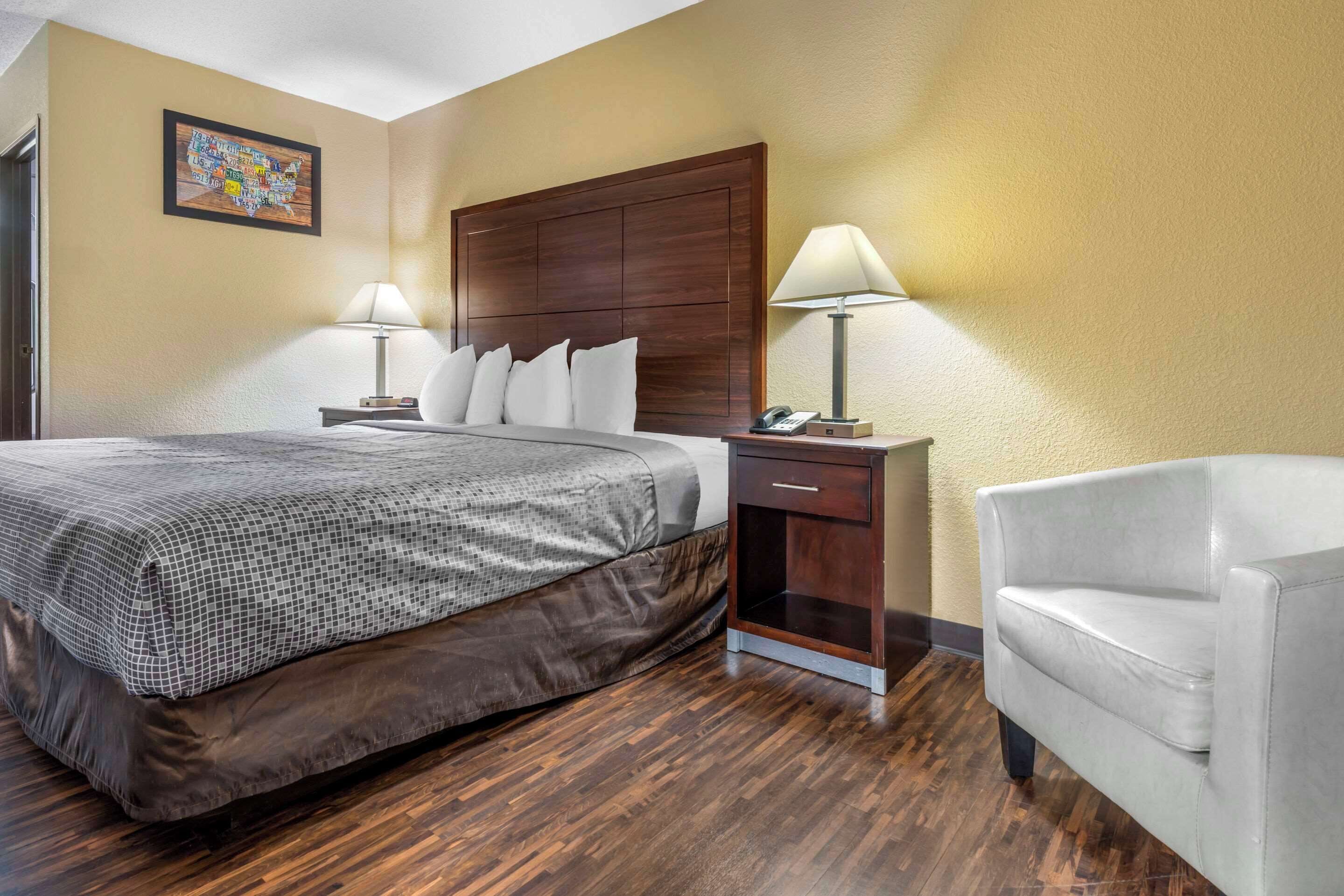 A hotel room with a large bed, two bedside tables with lamps, a chair, and a wooden headboard.