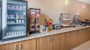 Zona de desayuno autoservicio con mostrador refrigerado, dispensadores de cereales, máquina de café y tostadora.