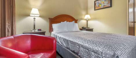 A hotel room with a bed, two bedside lamps, a red chair, a wooden headboard, and a wall map.