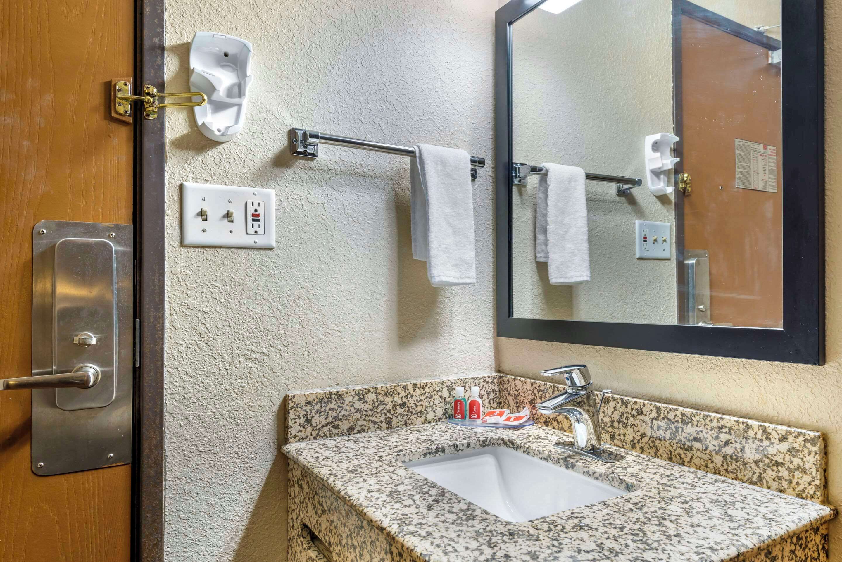 A bathroom with a granite countertop sink, a towel rack with two white towels, a mirror, and a wall-mounted electrical outlet.
